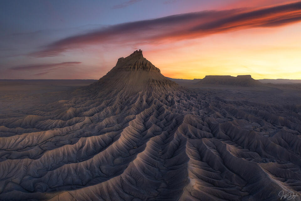 Factory Butte mesa rising above radiating badlands erosion channels beneath a dramatic sunset sky in the Utah desert