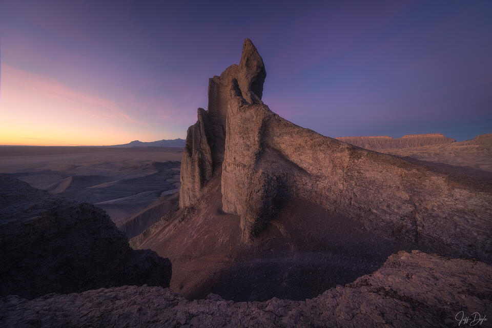Jagged sandstone spire at desert twilight with orange horizon glow and deep purple sky over Utah badlands