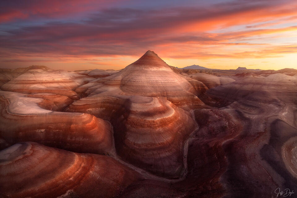 Striped bentonite cone rising from eroded desert floor at sunset with fiery sky over Utah high desert