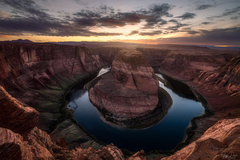 Horseshoe Bend at sunset with Colorado River curving through red canyon walls under warm desert sky