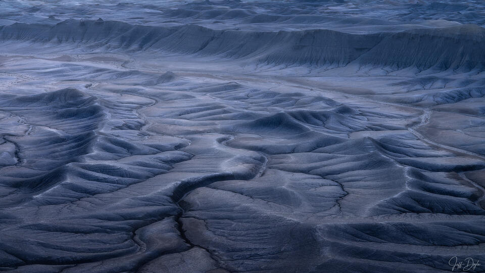 Blue-grey badlands below Moonscape Overlook in Utah, with rounded ridges, branching erosion channels, and deep blue shadows.