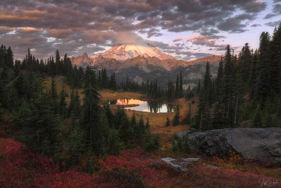 Autumn sunrise at Tipsoo Lake beneath Mount Rainier, red huckleberry foreground, reflective alpine lake, and clouds over the mountain. 