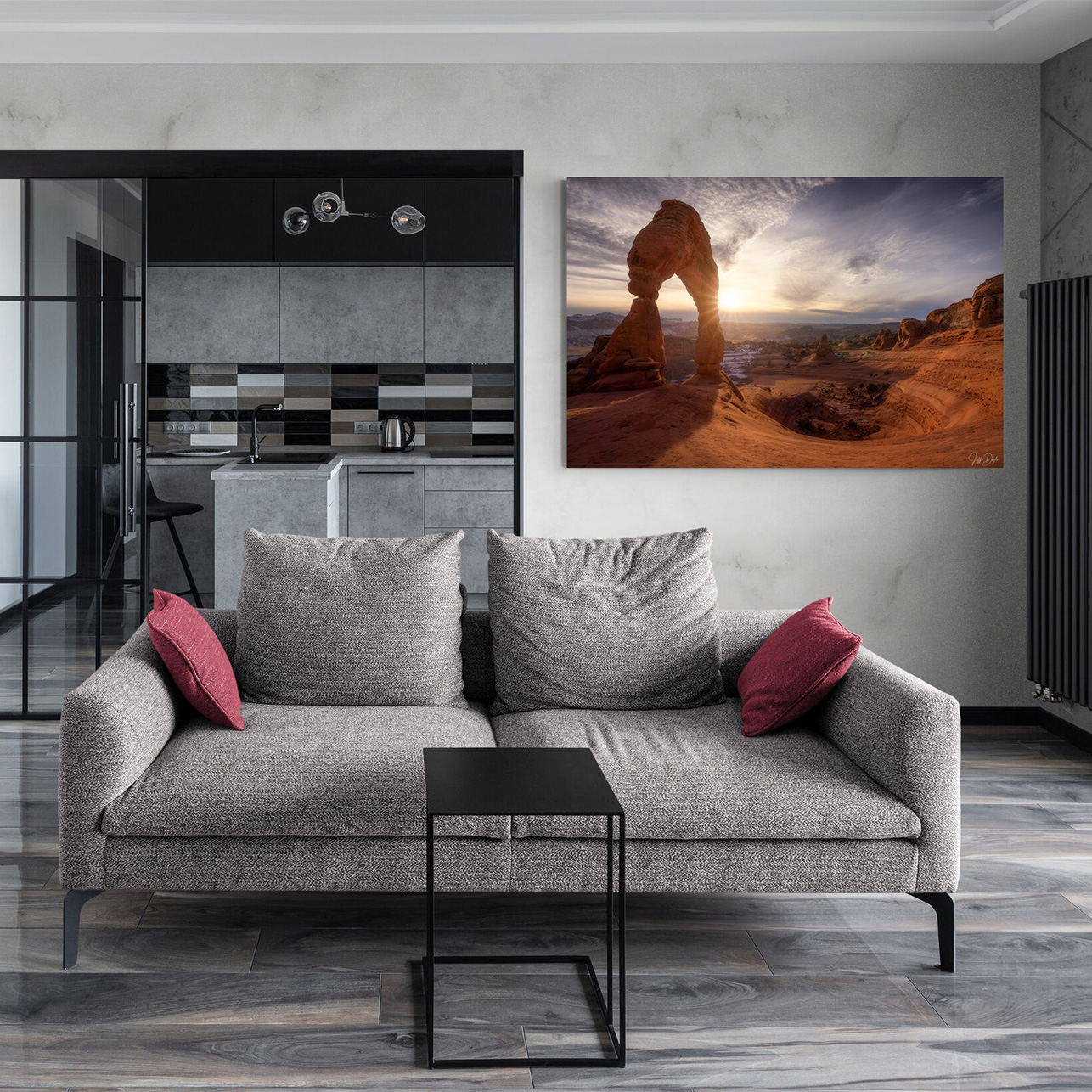 Modern luxury living room with gray sofa and red accent pillows featuring a large fine art landscape print of Delicate Arch at sunrise in Arches National Park, Utah displayed on a light wall above the couch.