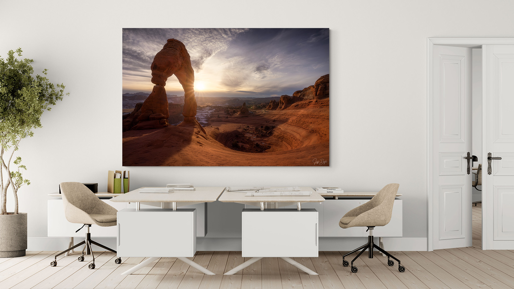 Modern home office interior with neutral furniture featuring a large fine art landscape print of Delicate Arch at sunset in Utah displayed above a white desk.